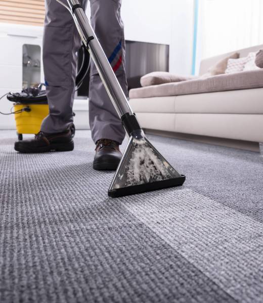 Low Section Of A Person Cleaning The Carpet With Vacuum Cleaner In Living Room